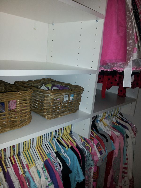 Walk-in closet with white shelves, wicker baskets, and colorful clothes hanging below.