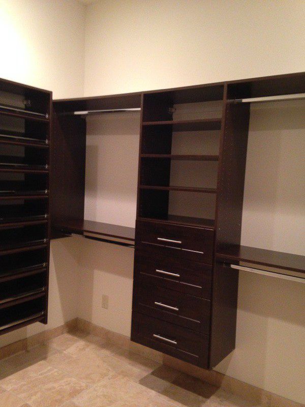 Built-in dark wood closet shelving and drawers in a beige room