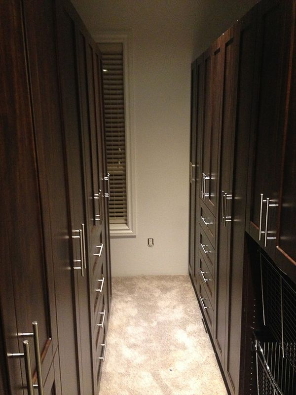 Narrow hallway between dark built-in closets with a window at the end, carpeted floor.