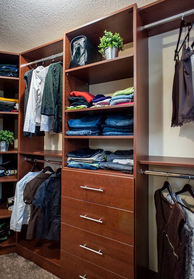 Wooden walk-in closet with hanging clothes, folded shirts, drawers, and empty shelves.