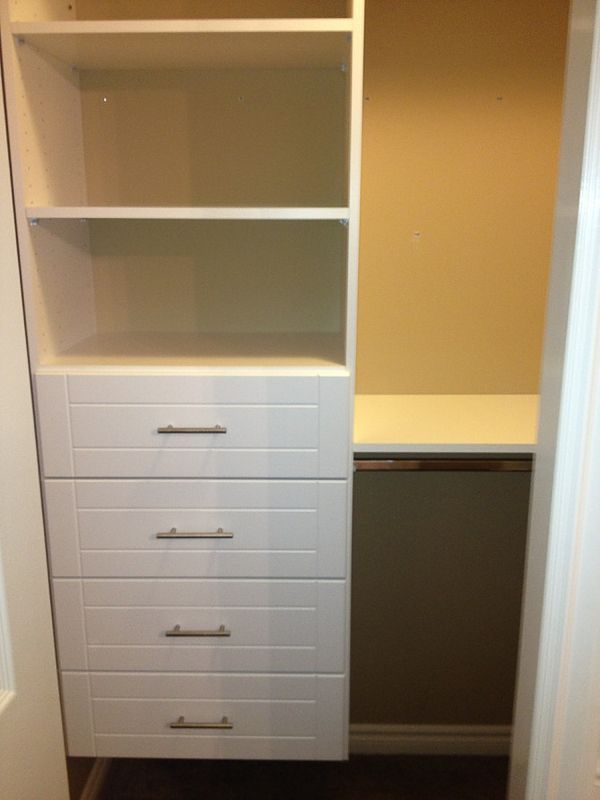 White built-in closet with shelves, drawers, and hanging space in a beige room.