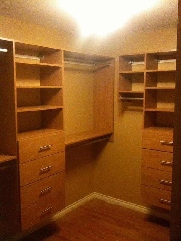 Walk-in closet with wooden shelves, drawers, and hanging rods under warm ceiling light