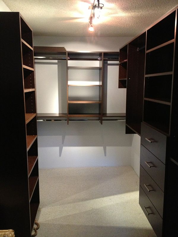 Walk-in closet with dark shelving, drawers, and hanging space, viewed from the doorway.