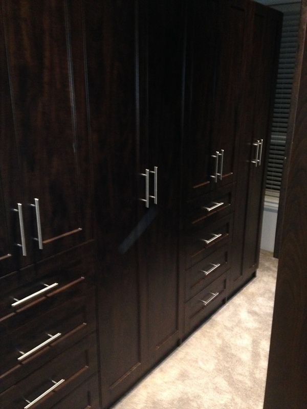 Dark wood bedroom wardrobe with silver handles and drawers along a beige carpeted floor.