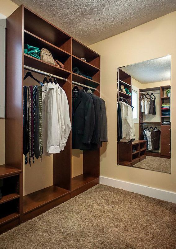 Walk-in closet with wooden shelves, hanging clothes, and a wall mirror on beige carpet.