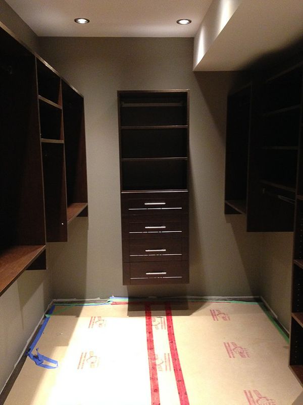 Walk-in closet with dark shelving, central drawers, and carpeted floor under recessed lights