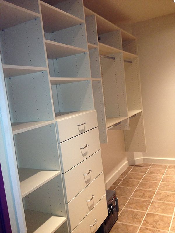 Built-in white closet shelving with drawers and hanging space in a tiled walk-in closet.