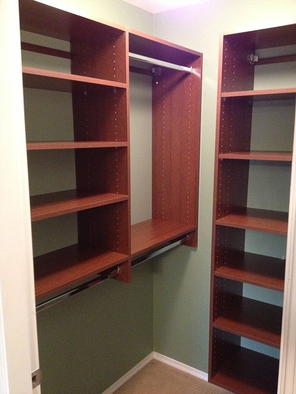 Empty walk-in closet with brown built-in shelves and hanging rod above green walls.