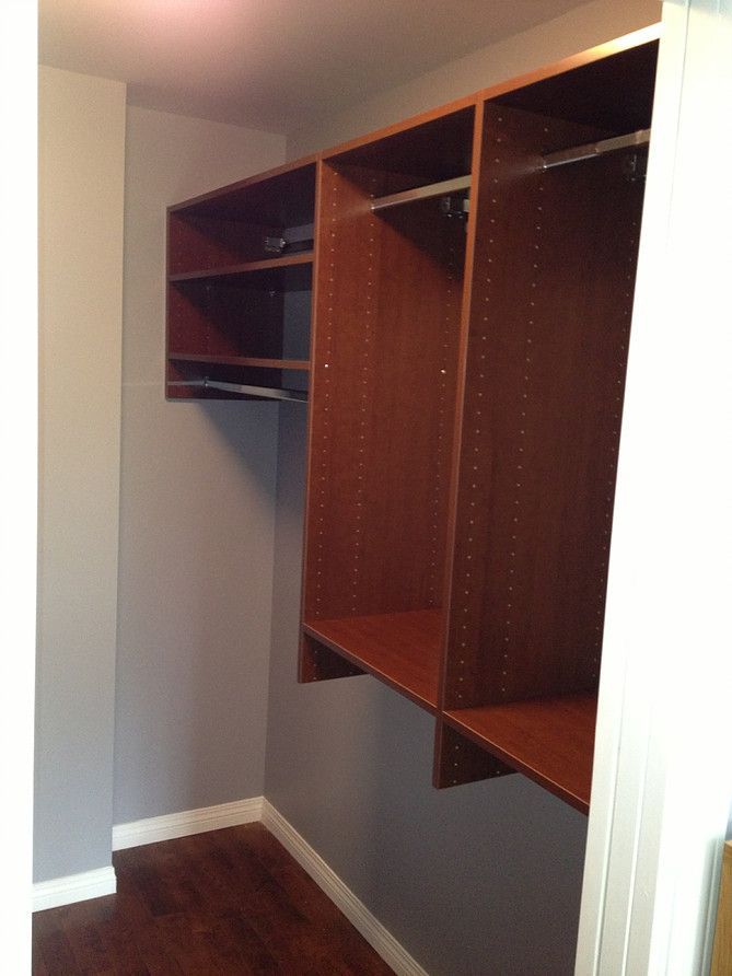 Empty walk-in closet with dark wood shelving and hanging rods on gray walls.