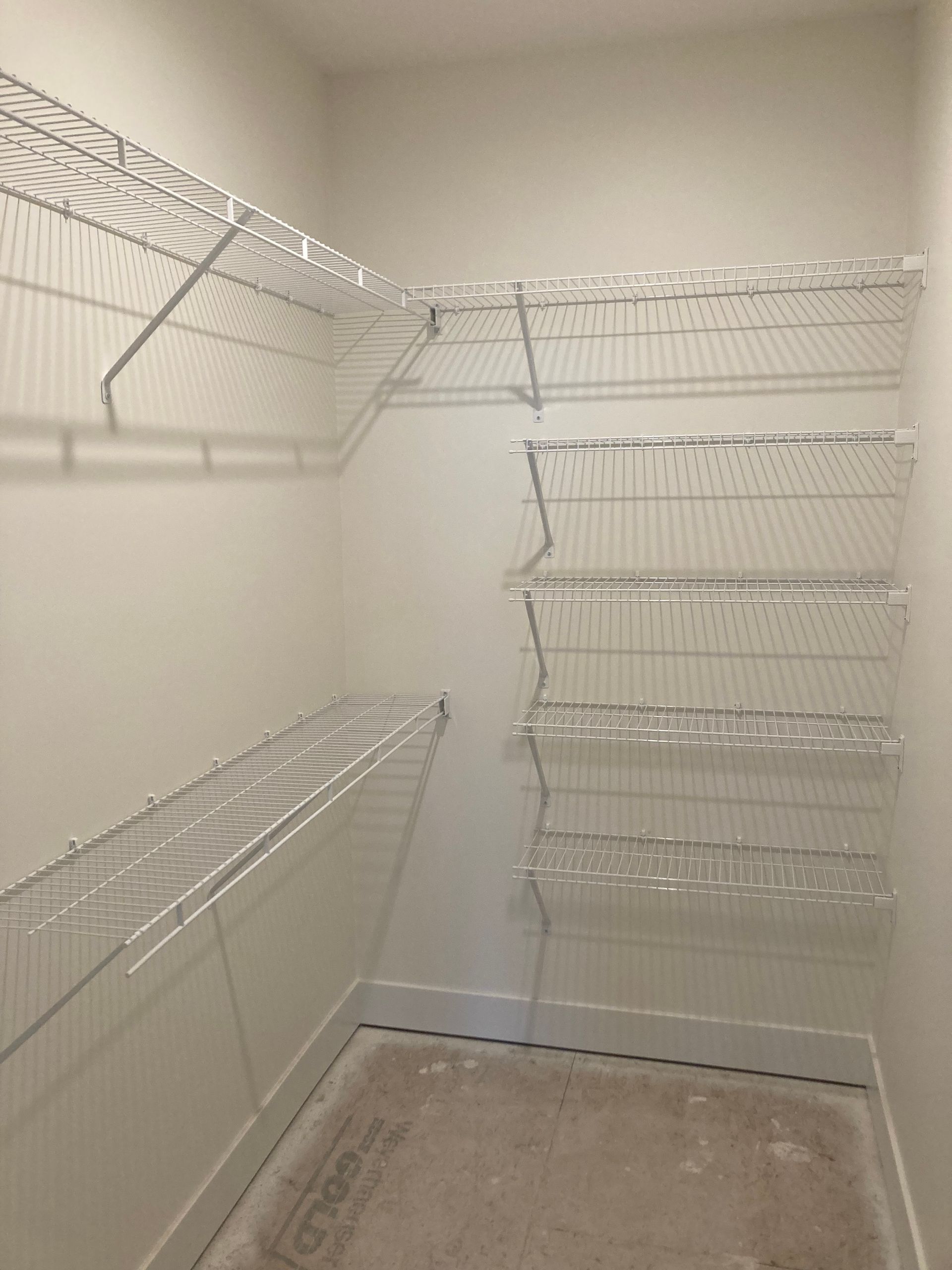 Empty walk-in closet with white wire shelving on both sides and beige carpet.