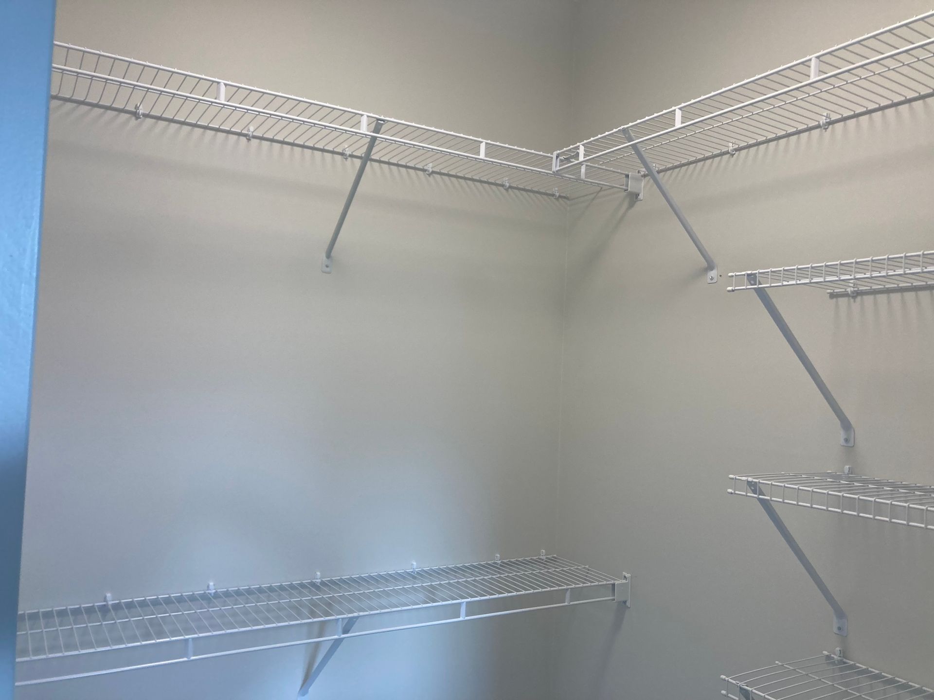 Empty wire closet shelves with metal supports on a white wall