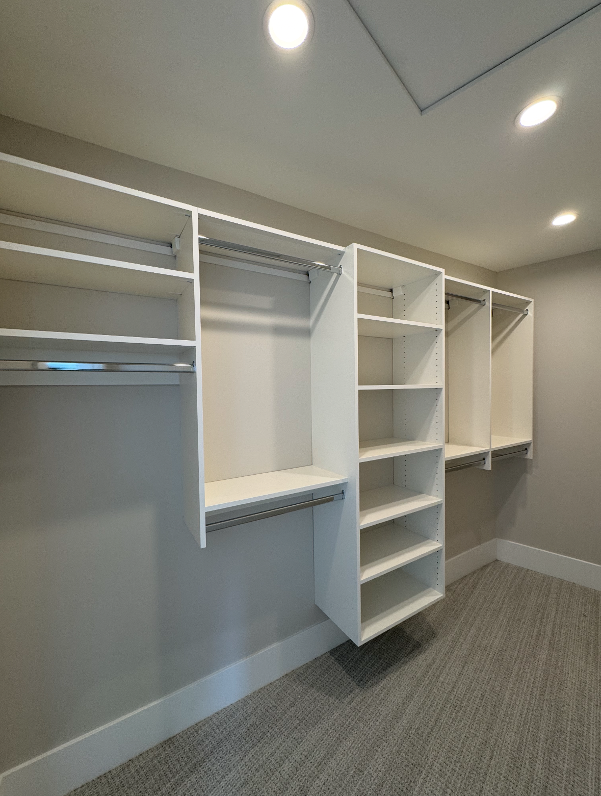 Empty walk-in closet with white shelving, hanging rods, and a carpeted floor under recessed ceiling lights