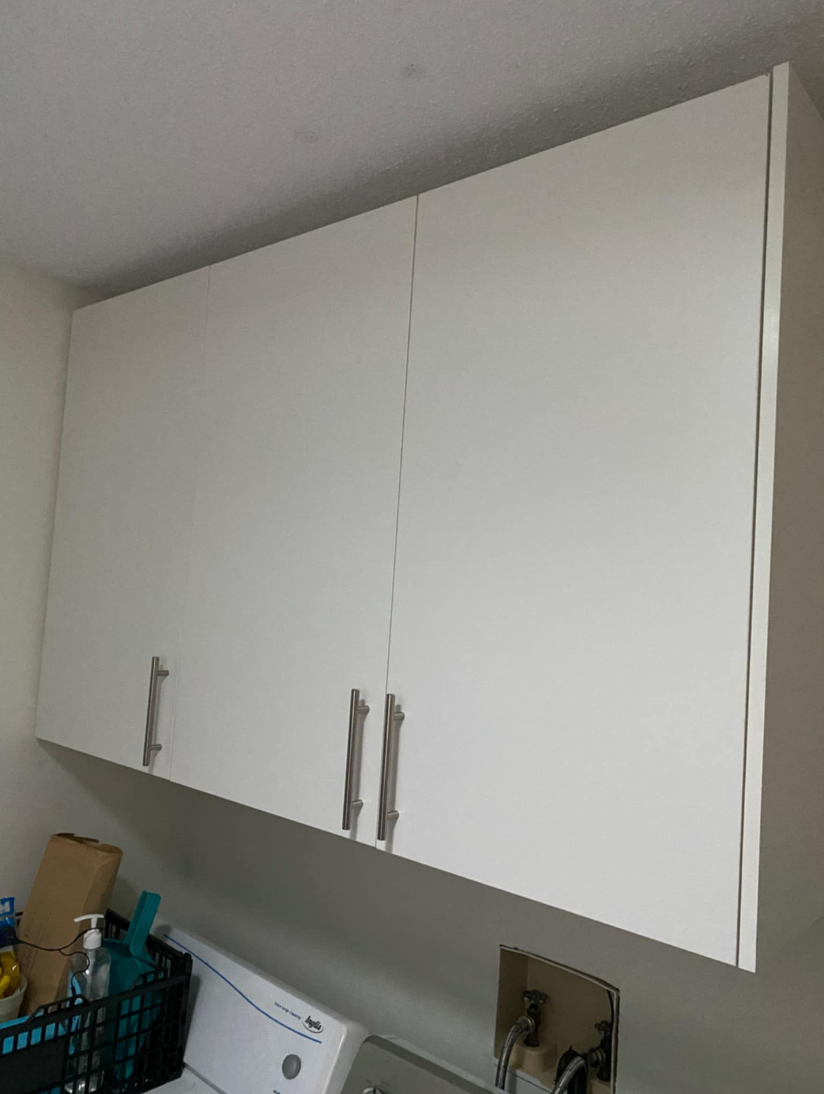 White kitchen wall cabinets above a countertop, with metal handles and a slanted ceiling