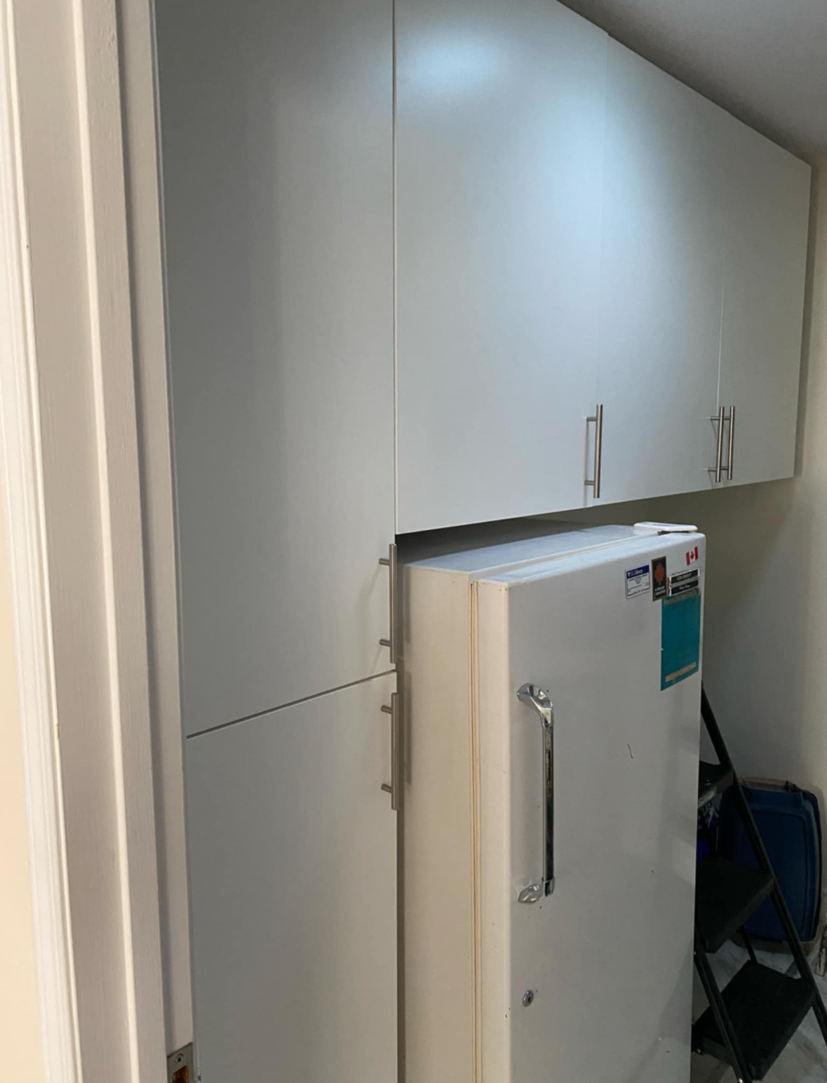 White refrigerator under slanted cabinets in a small storage room