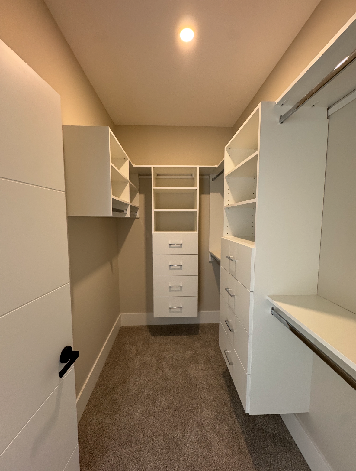 Walk-in closet with white shelving, drawers, and beige carpet under recessed lighting