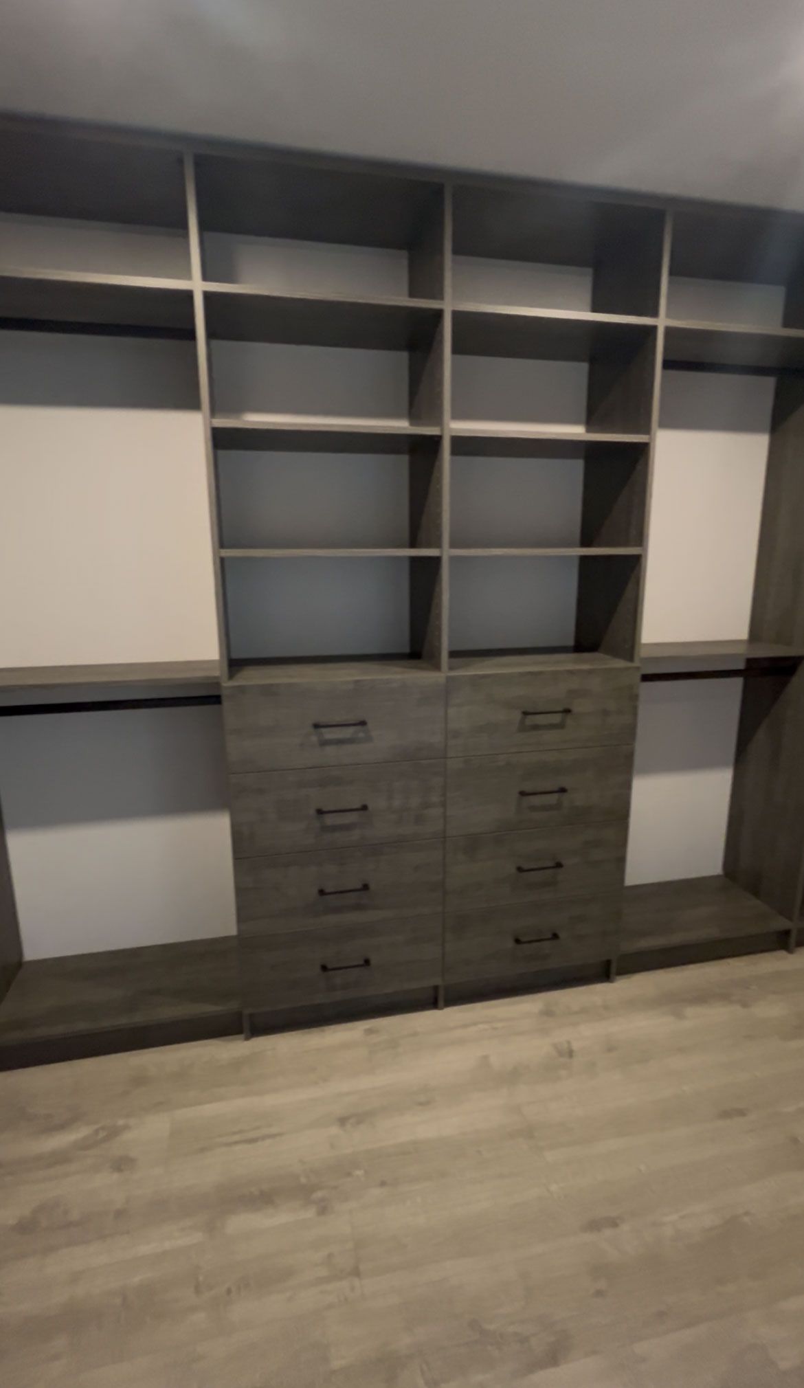 Built-in closet with gray shelves, drawers, and hanging sections in a room with light wood flooring