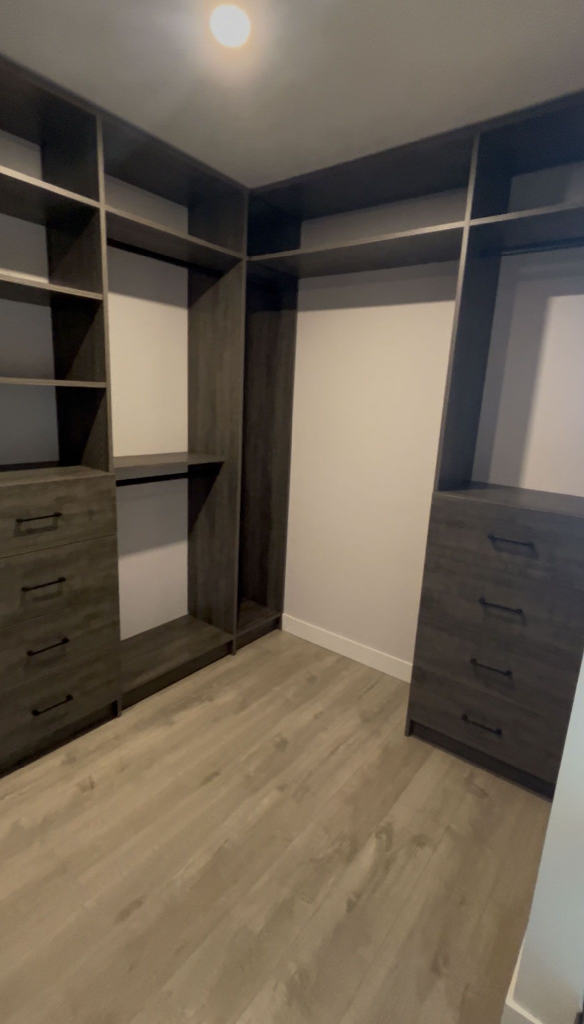 Walk-in closet with dark shelving, drawers, and wood flooring