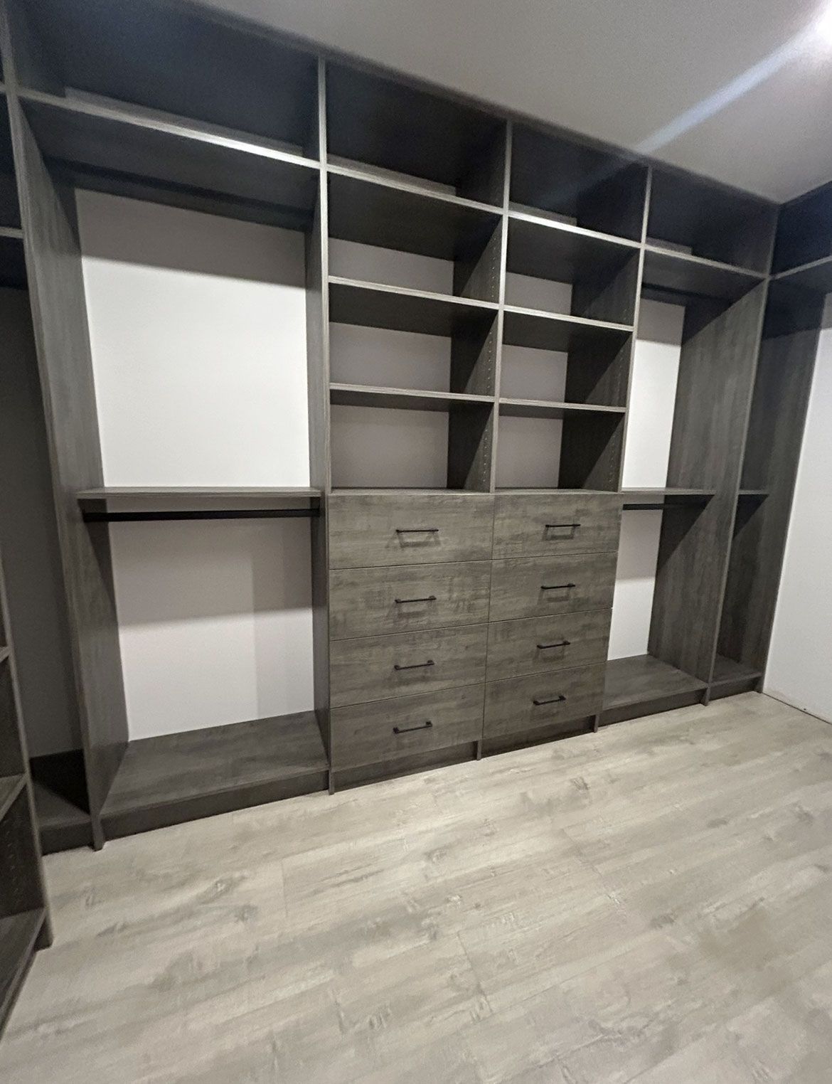 Built-in gray wardrobe with open shelves, drawers, and white accent panels in a modern room.