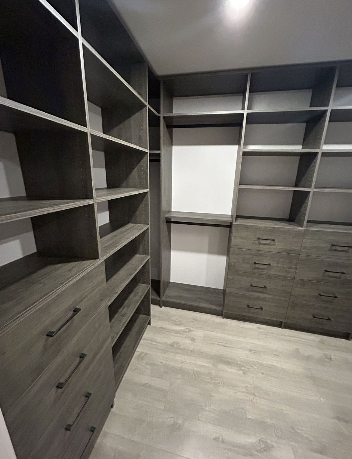 Walk-in closet with gray built-in shelves, drawers, and a light wood floor