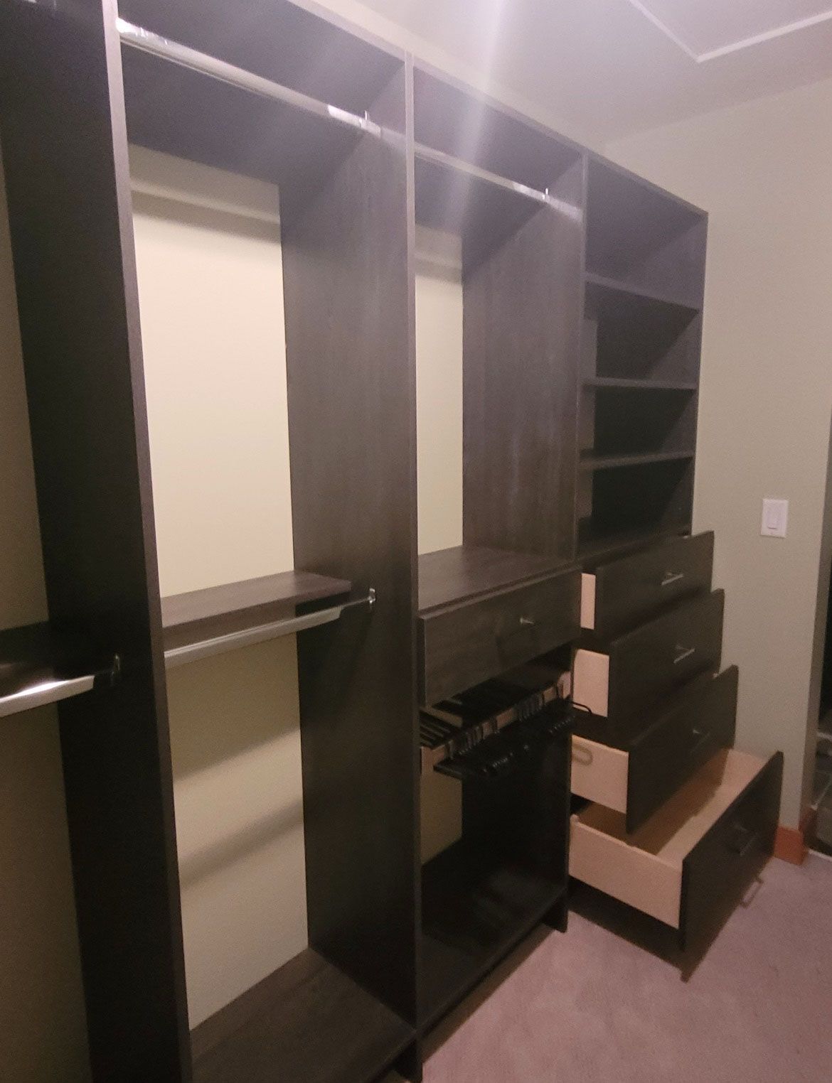 Dark wood walk-in closet with hanging rods, shelves, and several drawers, one drawer left open.