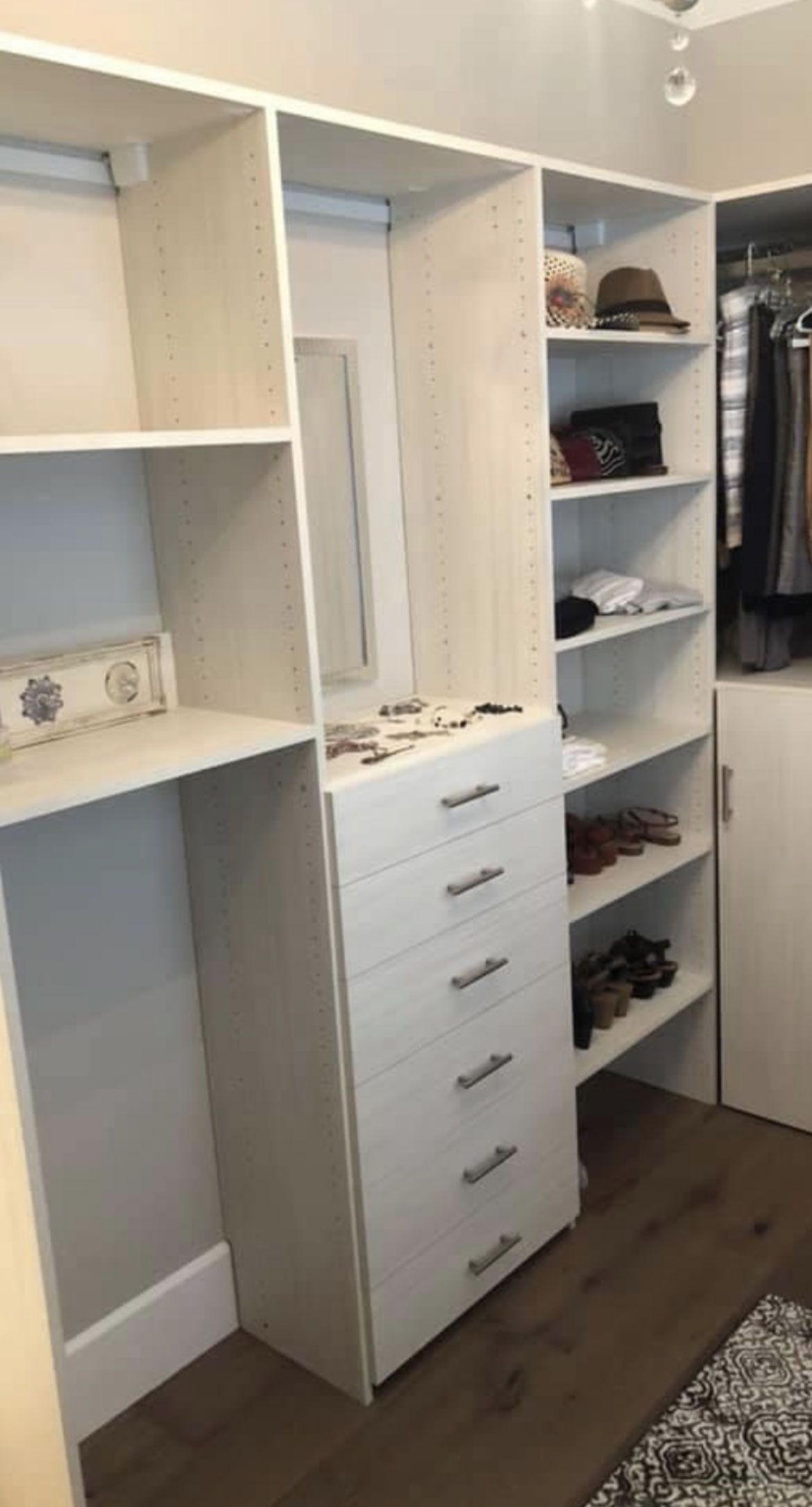 Open closet with white shelving, drawers, and hanging clothes in a bedroom.
