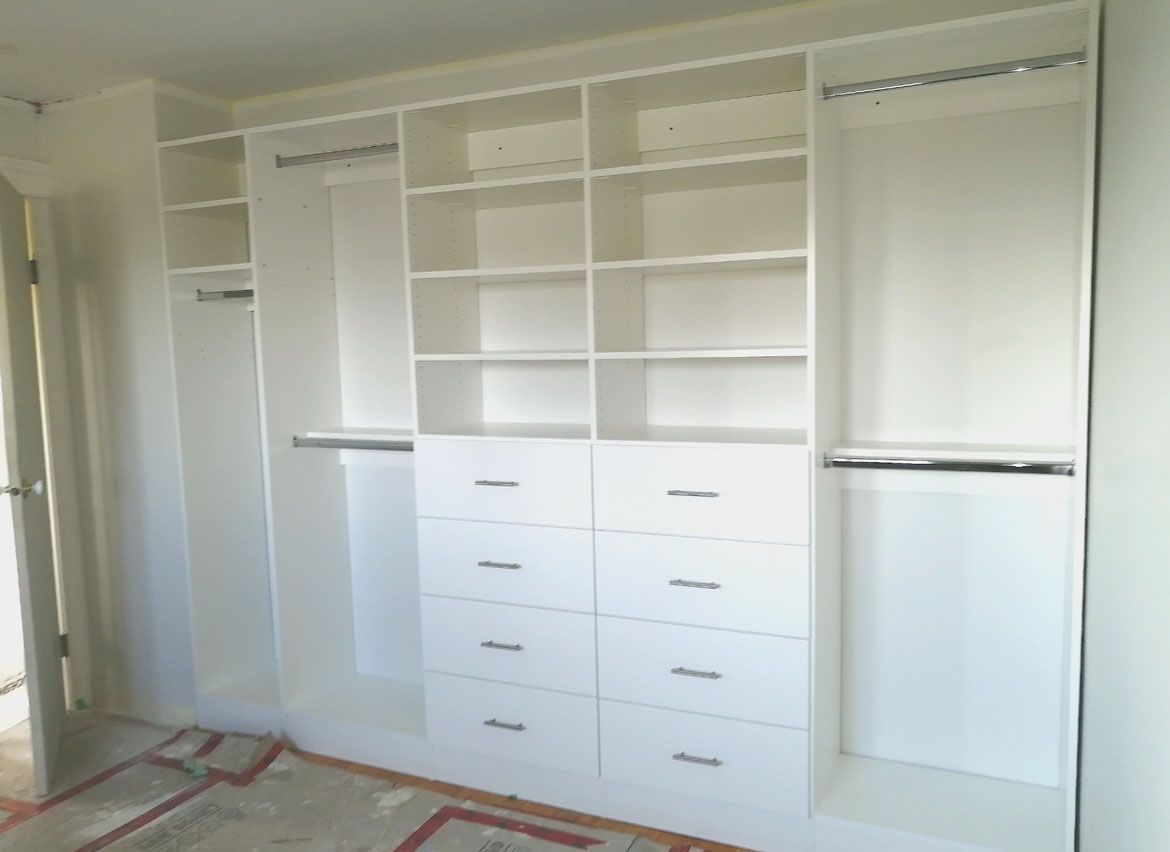 White built-in closet with open shelves, drawers, and hanging rods in an unfinished room