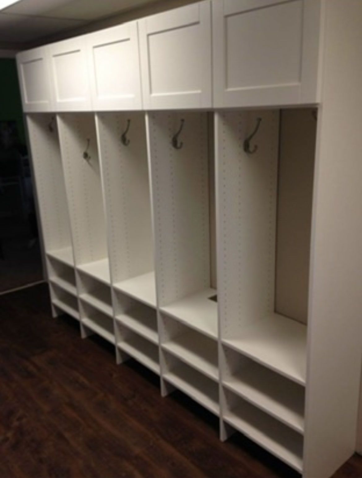 Empty white locker cubbies with hanging hooks in a room with dark wood flooring