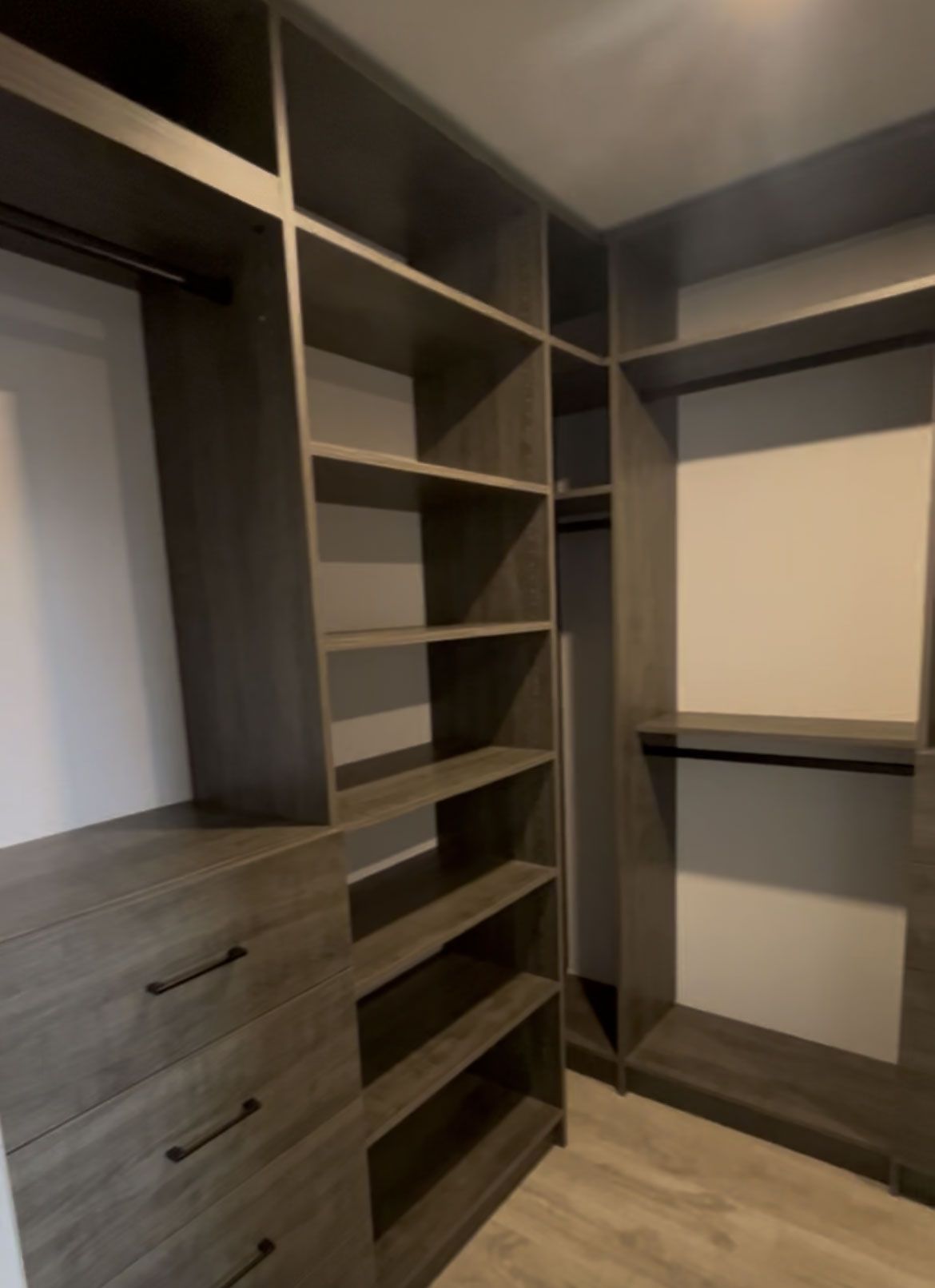 Empty walk-in closet with dark wood shelves, drawers, and hanging rods.
