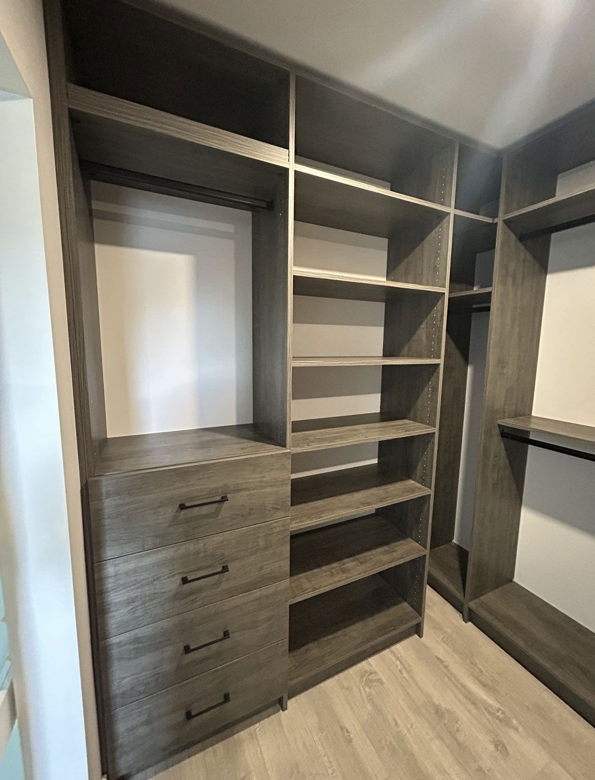 Built-in closet with dark wood shelves, drawers, and hanging space in a light room