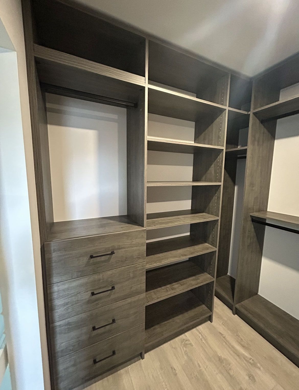 Built-in walk-in closet with dark wood shelving, drawers, and hanging spaces on a light wood floor.