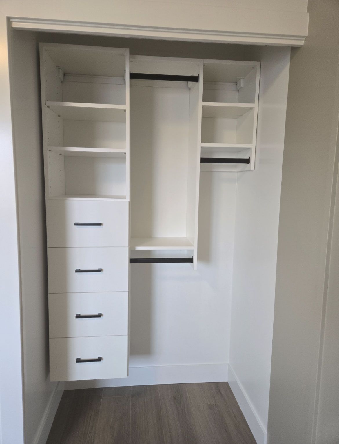 Open closet with white shelves, hanging space, and drawers in a small room with wood flooring.