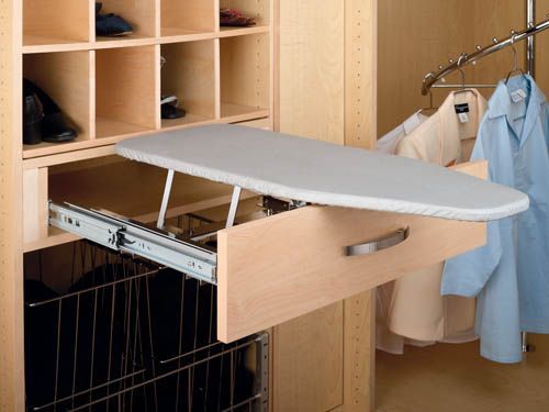 Pull-out closet ironing board with gray cover, extended beside hanging clothes and shelves