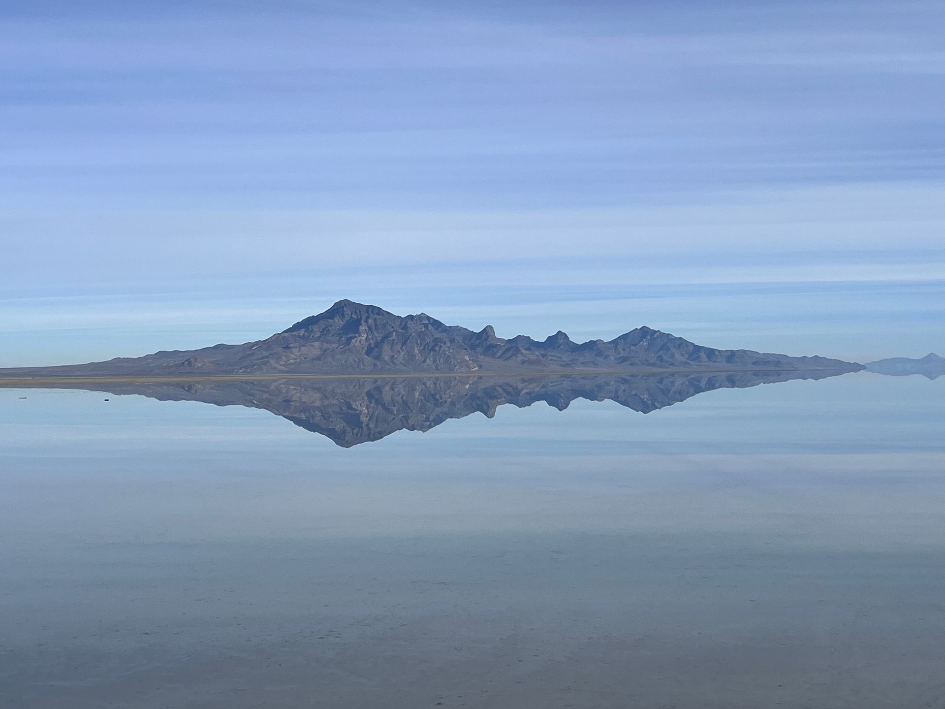 Mountain range reflected in still water, under a blue sky.