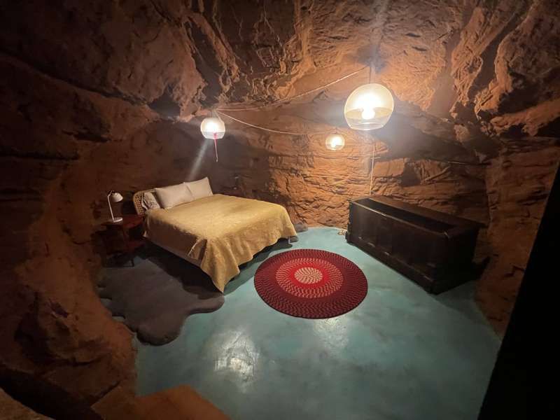 A lantern-lit cave bedroom with a queen bed and red rug