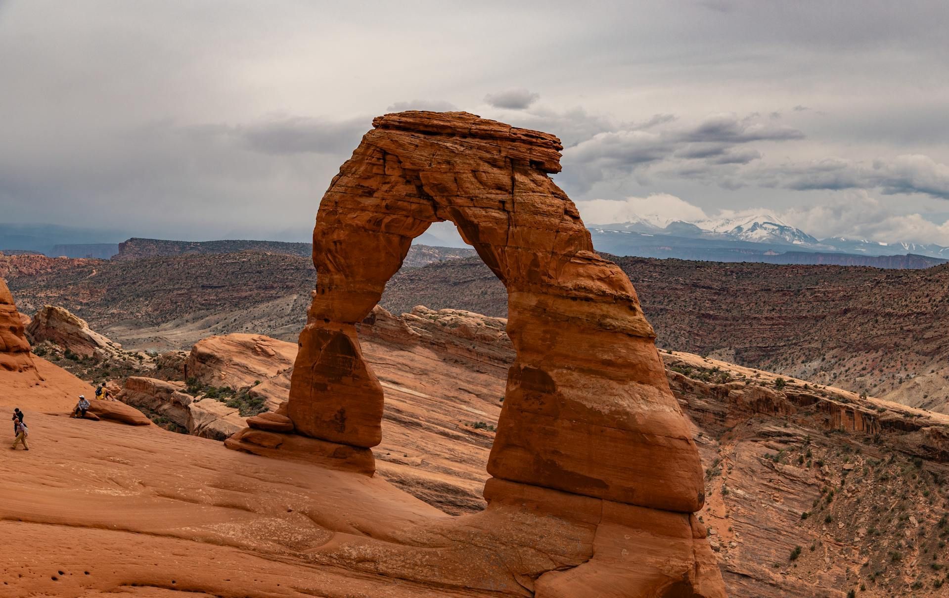 Delicate Arch in Arches National Park, Utah; sandstone arch against a cloudy sky, with distant mountains.