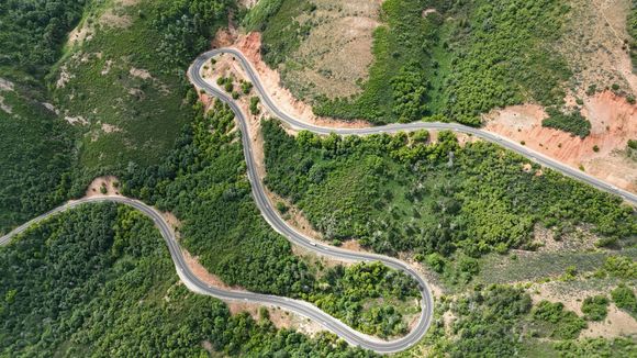 Aerial view of a winding road through a green, forested mountain landscape.