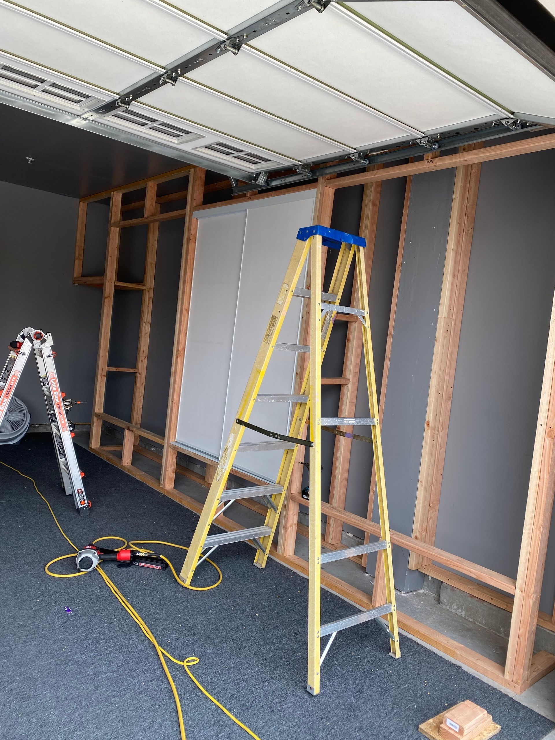 Garage interior with wood framing and drywall; a yellow ladder stands against a wall.