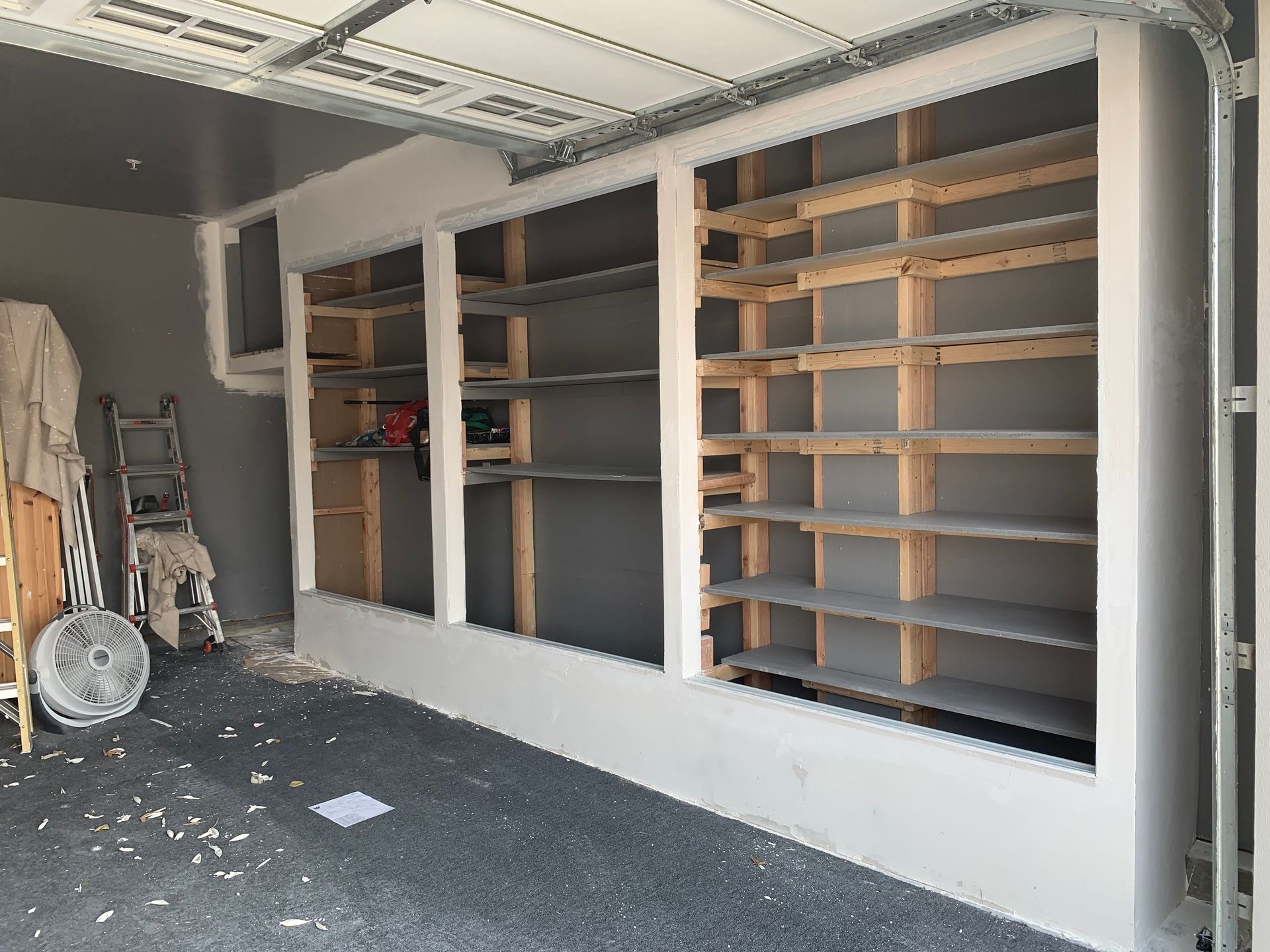 Garage with wooden shelving and drywall construction. Gray walls and flooring.