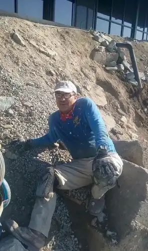 Man in blue shirt and white cap, working on a rocky hillside.