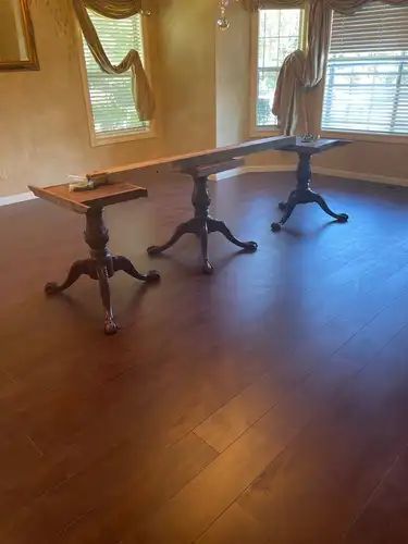 Three wooden pedestal tables on a wood floor in a room with windows and curtains.
