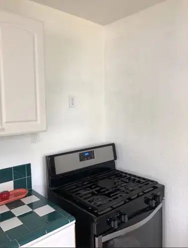 Black and silver gas stove in a white-walled kitchen corner, next to white cabinets and green tile counter.