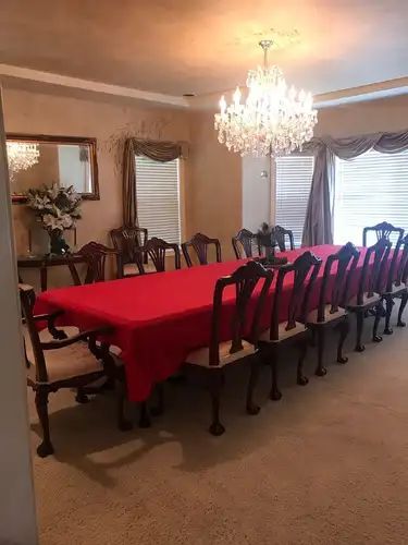 Formal dining room with long table set for many guests, red tablecloth, chandelier.