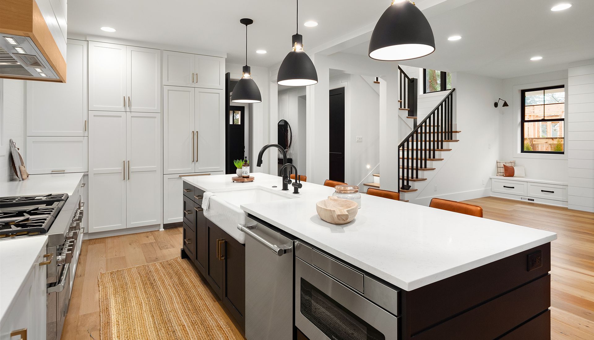 Modern kitchen with white countertops, dark island, stainless steel appliances, and wooden floors.