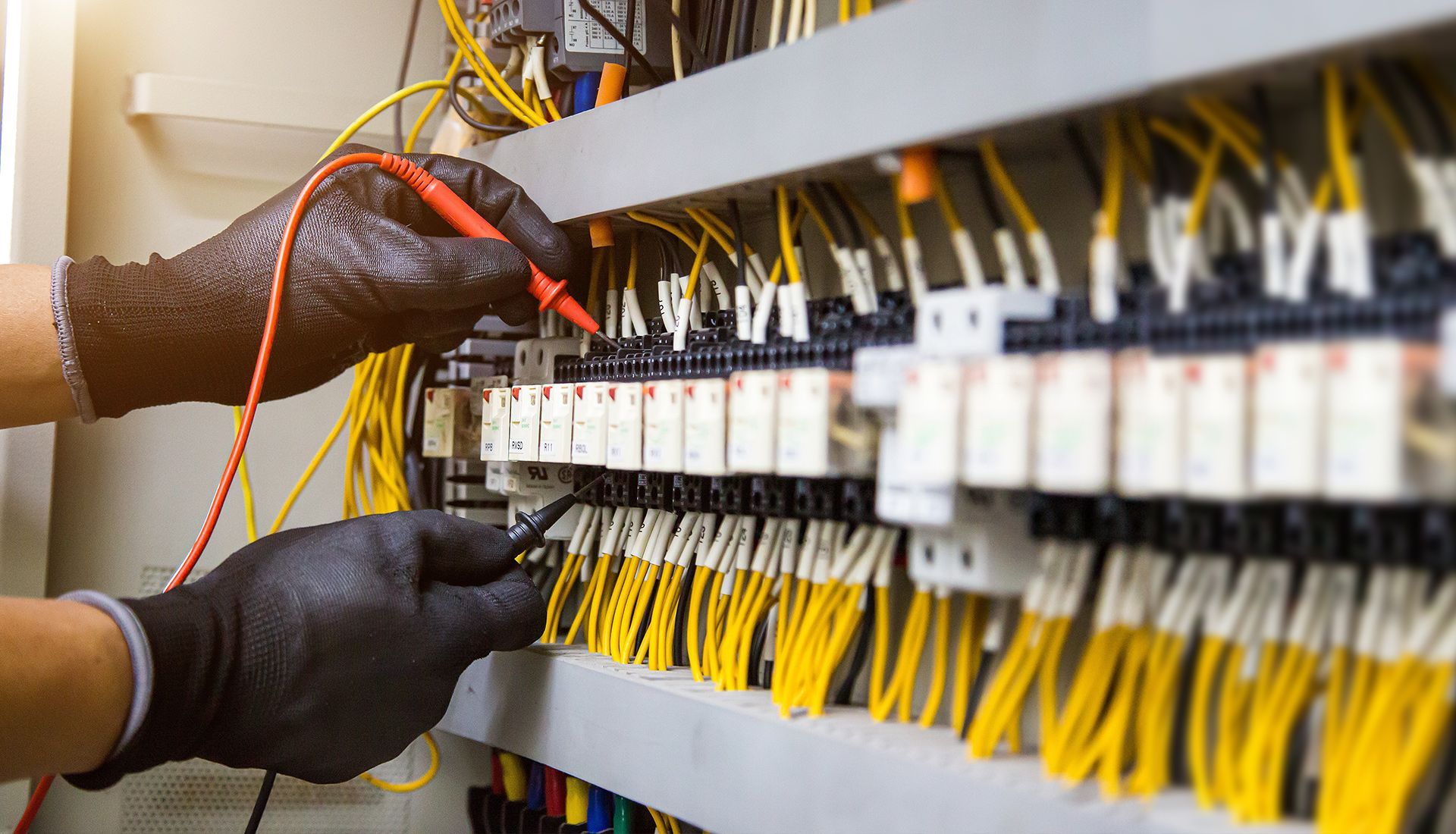 Hands in black gloves testing electrical wiring in a panel.