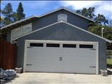 Garage with white door and dark blue siding, with a second story and small window.