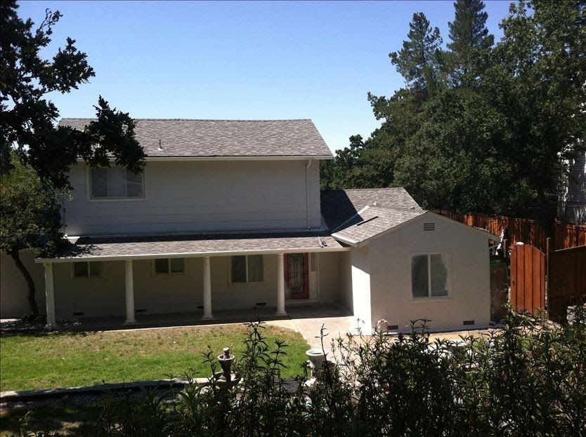 Two-story white house with a porch. Green lawn and trees surround the home under a blue sky.