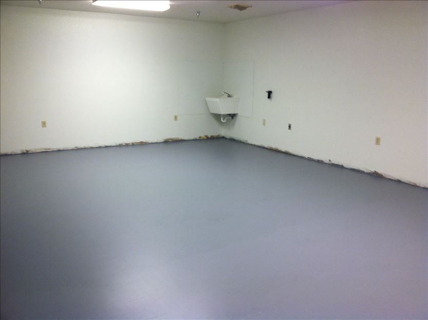 Empty room with pale blue floor and white walls. A sink is in the corner.