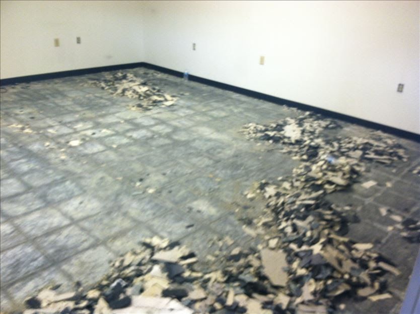Room with ripped up flooring, white walls, and scattered debris.