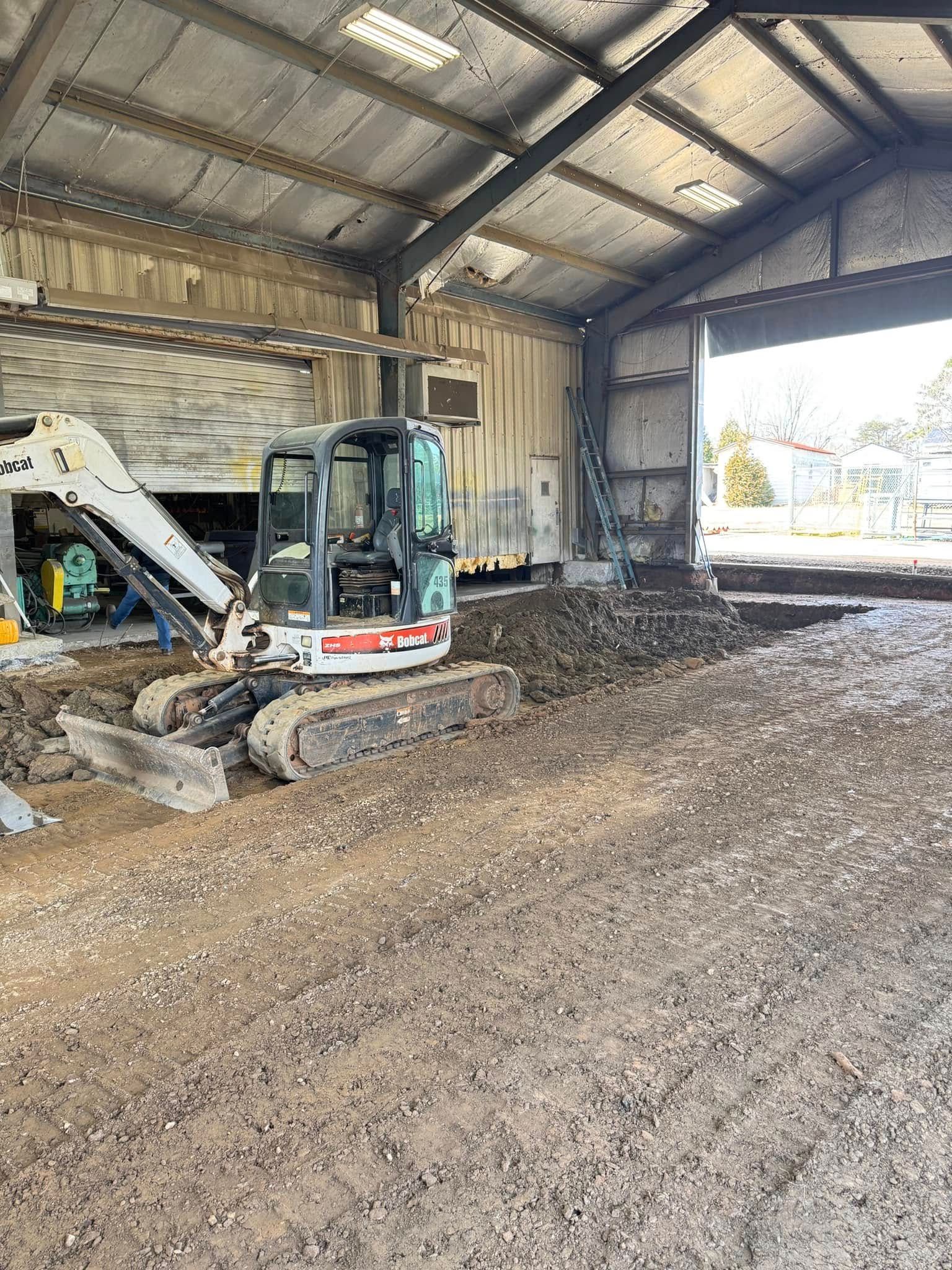 A small excavator inside a building, working on a dirt floor.