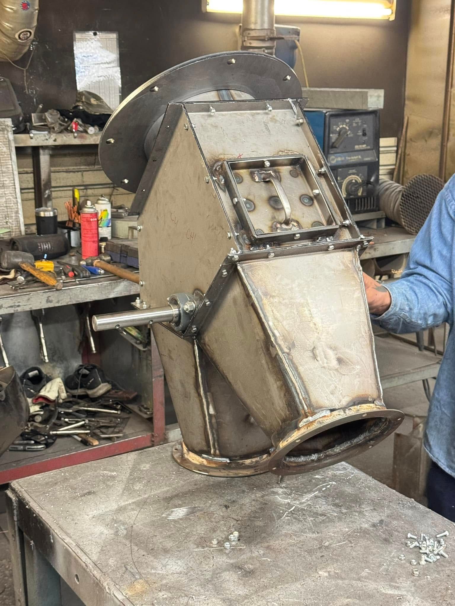 Metal industrial fabricated component on a workbench. A person is holding it in a workshop.